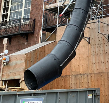 External chute on a construction site feeds a dumpster on the ground